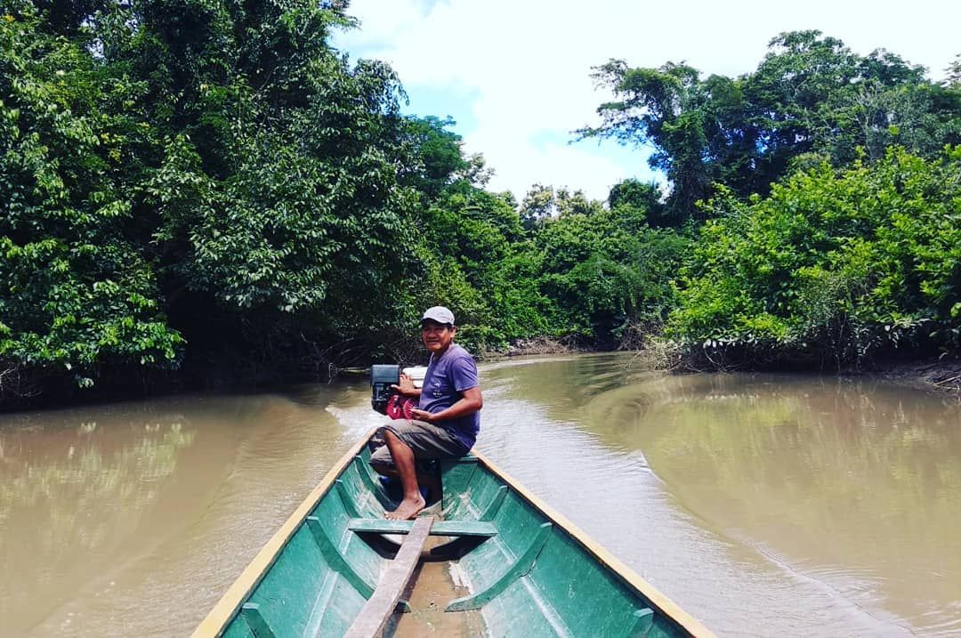 Canoe on brown river, tiny people, at Ampiri.