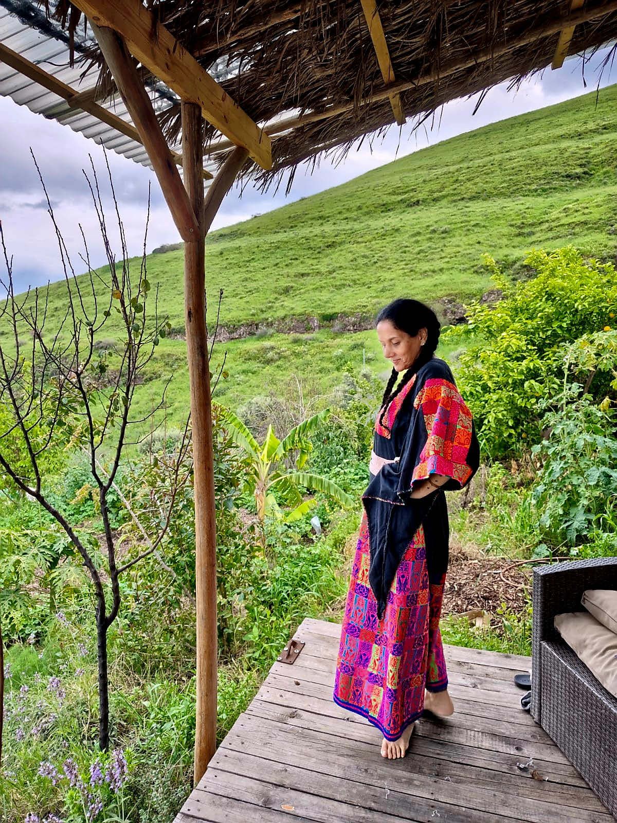 Doris on a wooden deck above a green hillside, in a pink and black wrap.