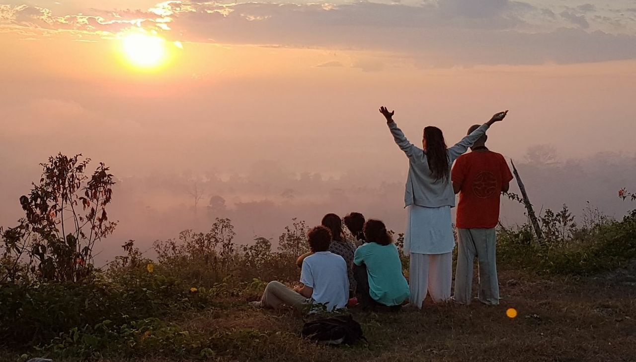 A small group on the hill at sunrise above the mist, two standing with arms raised.